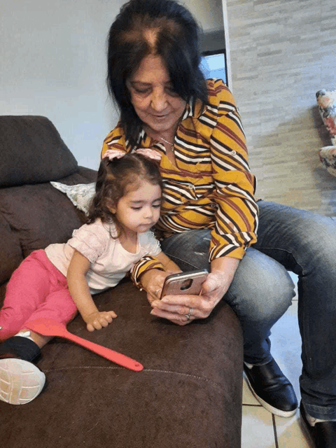 a woman sitting on a couch with a little girl looking at a phone