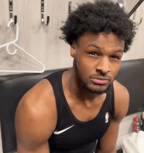 a man in a black tank top is sitting in a locker room with a hanger on the wall .