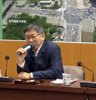 a man sitting at a table with a microphone in front of a wall with chinese writing