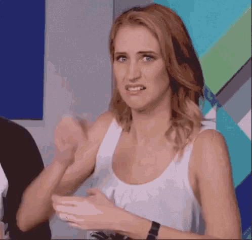 a woman in a white tank top is making a funny face with her hands .