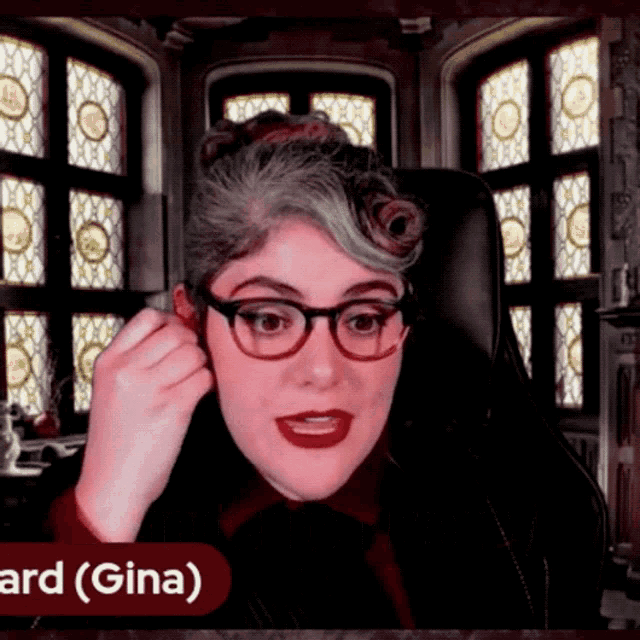 a woman wearing glasses is sitting in front of a window with the name gina on the bottom right
