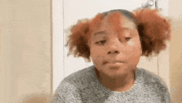 a young girl with red hair is making a funny face while wearing a sweater .
