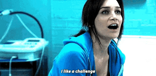 a woman in a blue sweatshirt is screaming and saying `` i like a challenge '' .