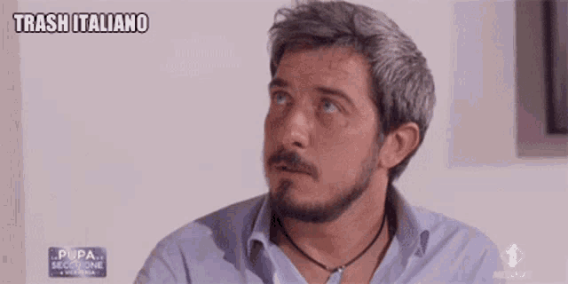 a man with a beard is wearing a blue shirt and a necklace and says trash italiano .