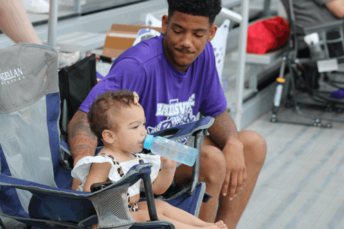 a man wearing a purple shirt that says raiders sits with a baby