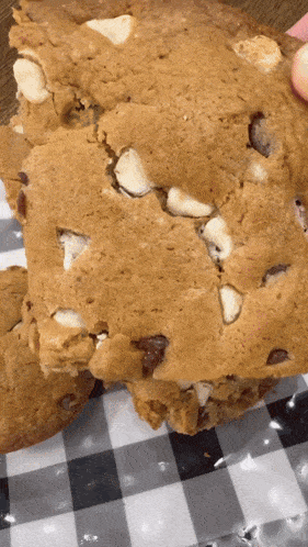 a close up of a cookie with white chocolate chips on a checkered cloth