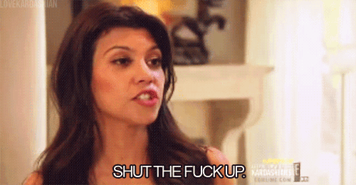 a woman is saying shut the fuck up while standing in front of a bookshelf .