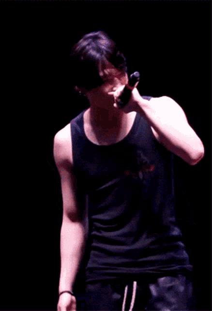 a man in a black tank top is holding a microphone in his hand