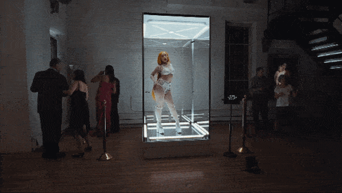 a woman in a white outfit is standing in a display case surrounded by people