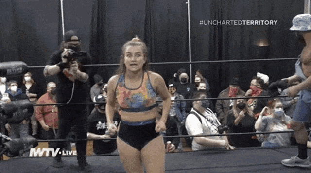 a woman in a tie dye top is standing in a wrestling ring with the words uncharted territory on the bottom