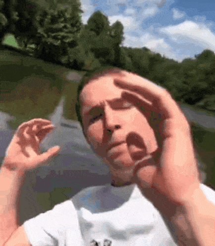 a man in a white shirt is making a funny face in front of a body of water .