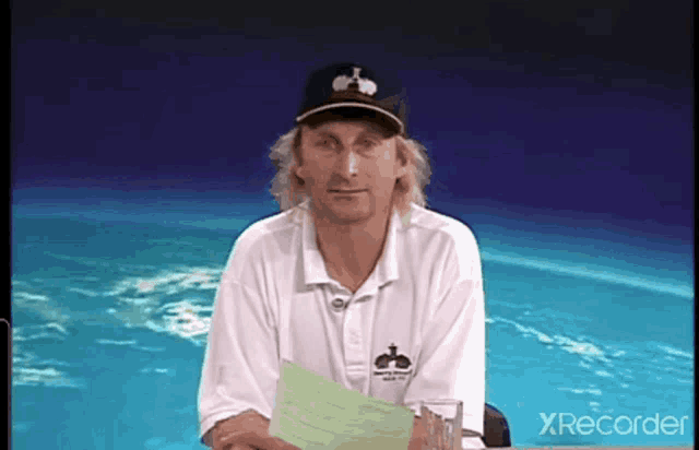 a man wearing a white shirt and a black hat is holding a piece of paper in front of a pool ..
