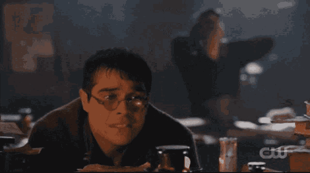 a man wearing glasses sits at a table with a cw logo in the corner