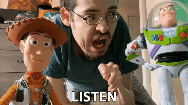 a man with glasses is standing next to a woody and buzz lightyear toy