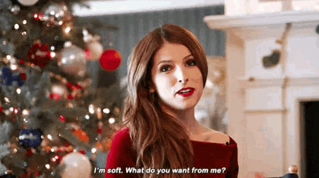 a woman in a red dress is standing in front of a christmas tree and talking .