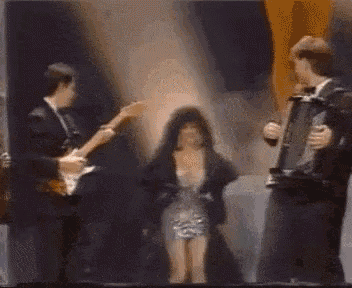 a woman in a dress is standing in front of two men playing instruments