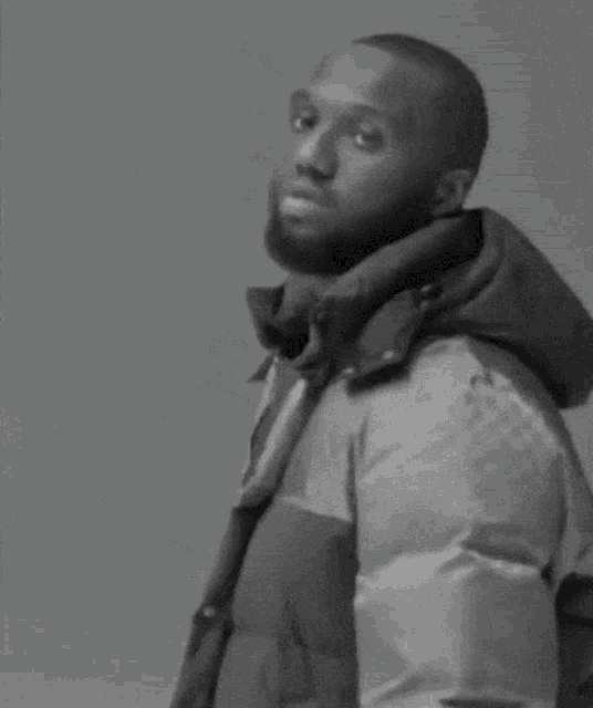 a black and white photo of a man wearing a jacket and a hood .