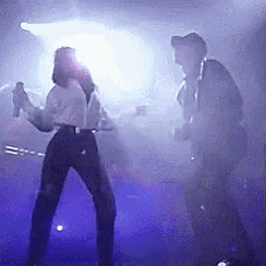 a man and a woman are dancing on a stage in a dark room with a blue light behind them .