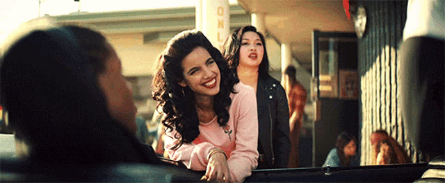 two women are sitting in a car in front of a building with a sign that says gnl