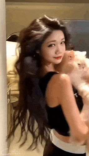 a woman with long hair is holding a cat in her arms in a room .