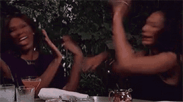 two women are sitting at a table with their hands in the air .