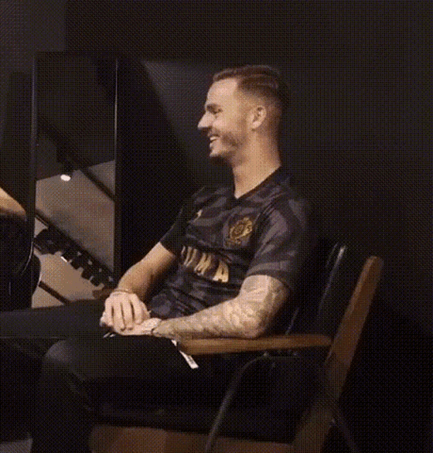 a man in a black shirt is sitting in a chair laughing .