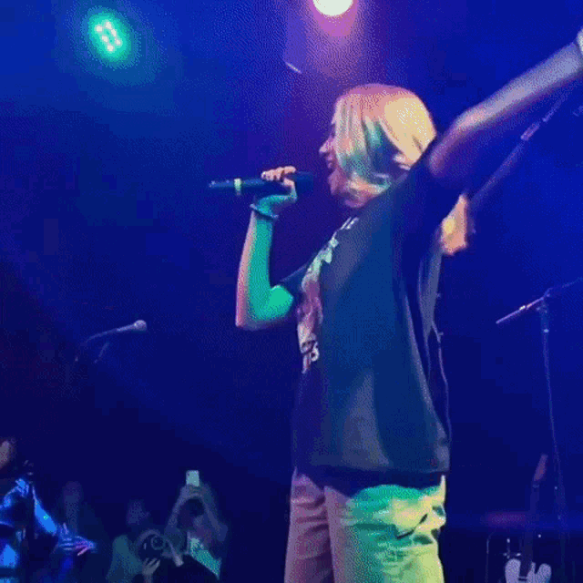 a woman wearing a t-shirt that says for the jomies is singing into a microphone on stage .