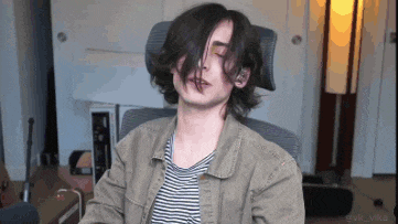 a young man with long hair is sitting in a chair with his eyes closed