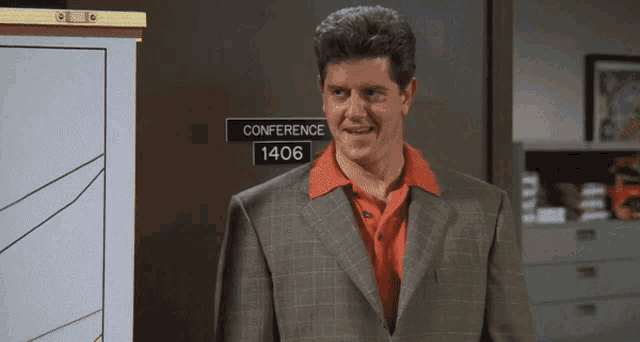 a man in a suit is smiling in front of a conference sign