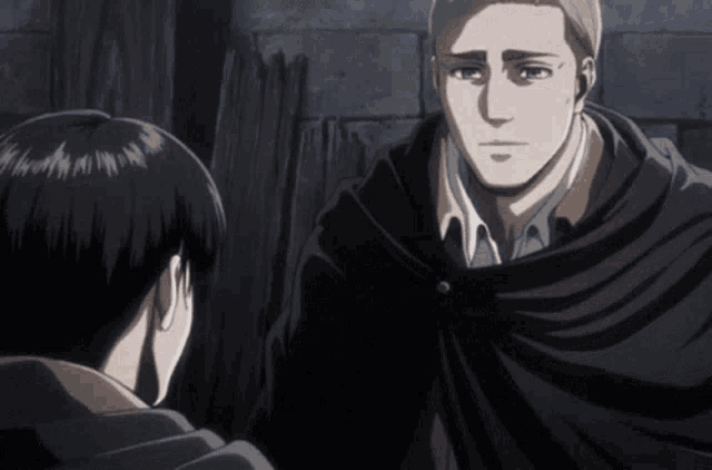 a man in a black cape talks to another man in a white shirt