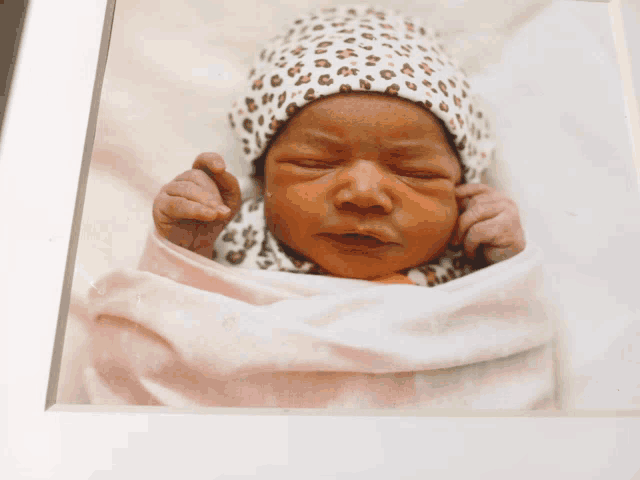 a baby wearing a leopard print hat and a pink blanket