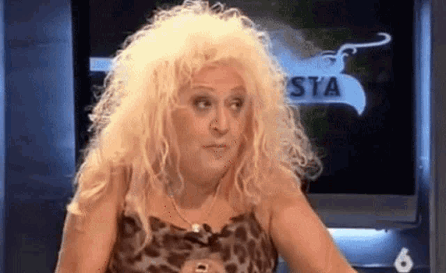 a woman with blonde hair and a leopard print dress is sitting in front of a television screen .