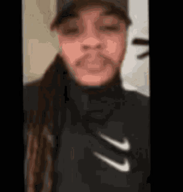 a man with dreadlocks is wearing a hat and a black nike jacket .