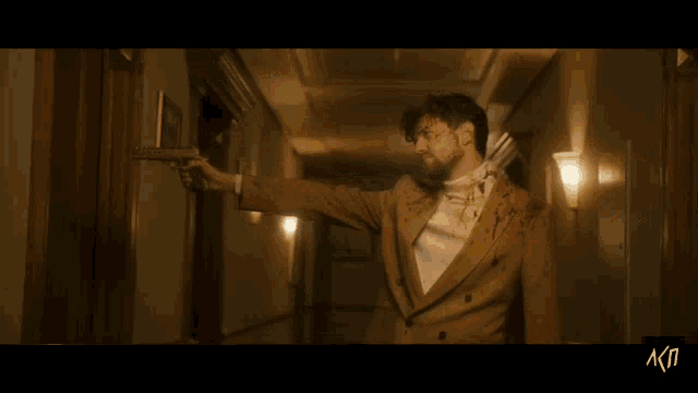 a man in a suit and tie is holding a gun in a hallway with the letters akp below him