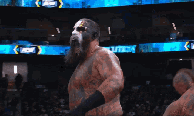 a wrestler with a beard and face paint stands in front of a aew sign