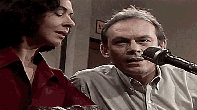 a man is singing into a microphone while a woman watches