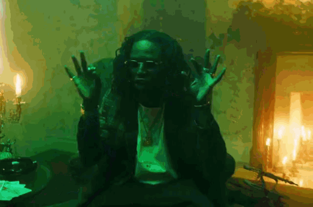a man with long hair and sunglasses is sitting in a dark room with candles