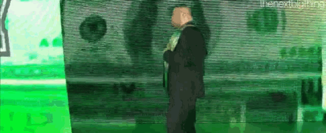 a man in a suit and tie is standing in front of a green wall .