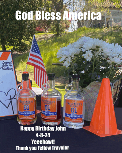 a bottle of moonshine sits on a table with flowers and an american flag