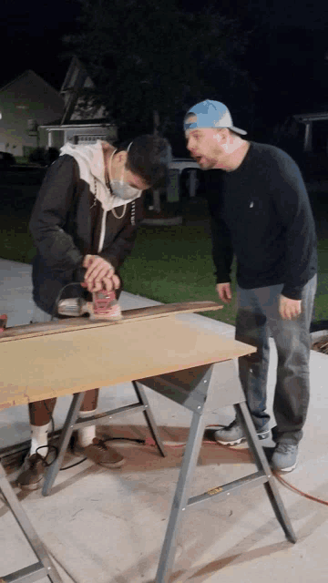 two men are sanding a piece of wood on a workbench