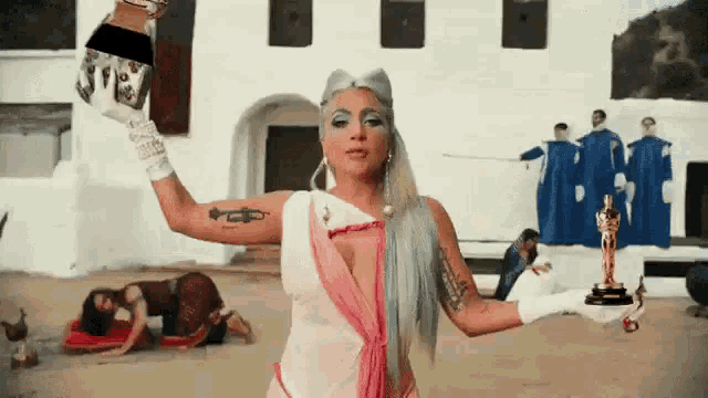 lady gaga is holding a trophy in her hand in front of a building .