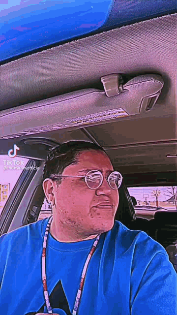a man wearing glasses and a blue shirt is sitting in a blue car .
