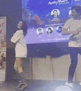 a man and a woman are dancing on a stage in front of a screen that says ayala