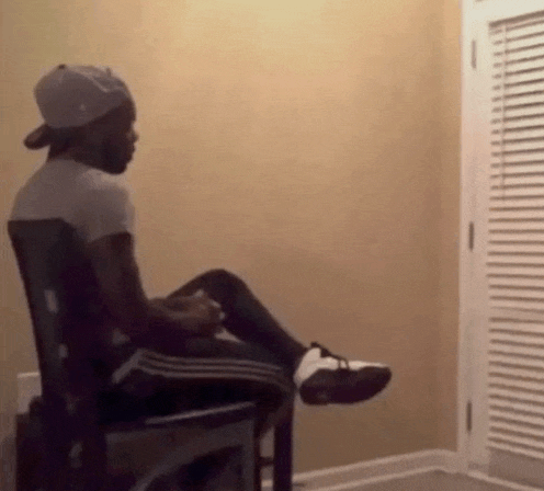 a man wearing a hat is sitting in a chair in a room with his legs crossed .