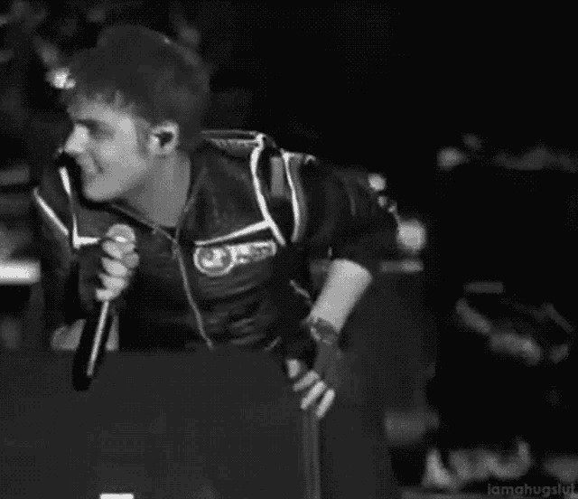 a black and white photo of a man singing into a microphone on a stage .