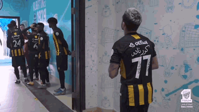 a man in a number 77 jersey stands in a hallway with other players