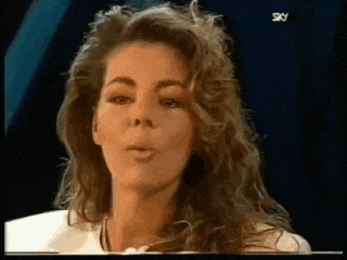 a woman with long curly hair is making a funny face and blowing a kiss .