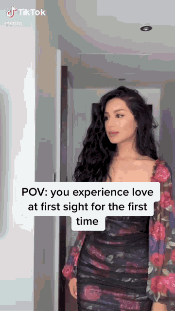 a woman in a floral dress is standing in a hallway with a tiktok video .