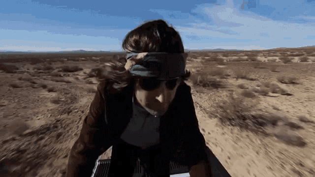 a man wearing sunglasses and a green headband rides a motorcycle in the desert