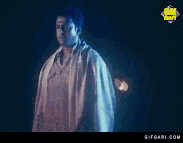 a man in a white robe is standing in a dark room with a blue background .